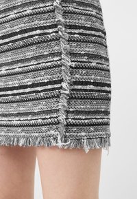 Jupe rayée en noir et blanc avec un design en tricot texturé et un ourlet effiloché. Le tissu présente une épaisseur variable dans les rayures.