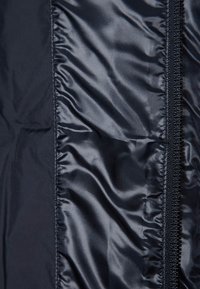 Černá zateplená bunda z látky, která má hladkou, lesklou texturu, boční zip a prošívané části pro zvýšení tepla.