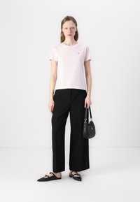 Tricou scurt roz din bumbac, cu guler rotund, asortat cu pantaloni largi negri și balerini negri. Un detaliu mic cu logo este vizibil pe tricou.