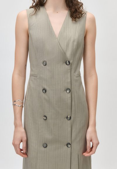 Φόρεμα διπλής σειράς με μπεζ λεπτές ρίγες χωρίς μανίκια, με μαύρα κουμπιά, συνδυασμένο με ασημένιο κυματιστό βραχιόλι στον αριστερό καρπό.