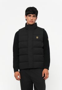 Black padded vest with high collar and golden logo. Features a quilted design, side zippers, and a fitted silhouette. Fabric appears smooth.