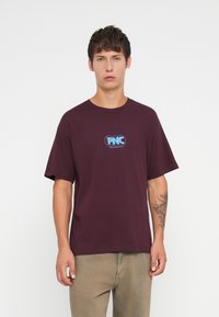 Maroon cotton t-shirt with short sleeves and a round neck. Features a blue graphic logo on the chest. Casual fit, soft texture.