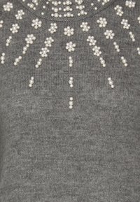 Maglione grigio a maglia con gruppi di piccole decorazioni bianche simili a perle disposte in motivi floreali sulla parte anteriore.