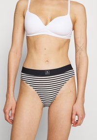 Svart og hvit stripete bikini-bunn med elastisk midjebånd som har en liten logo. Mykt stoff, klassisk snitt og glatt tekstur.