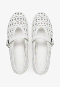 Bílé Mary Jane boty vyrobené z perforované gumy, s designem kruhových a trojúhelníkových výřezů a s popruhem na přezku pro bezpečné upevnění.
