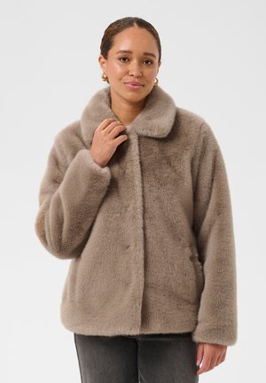Femme à la peau marron clair et aux cheveux tirés en arrière, portant des boucles d'oreilles créoles dorées et une veste en fausse fourrure taupe avec col.