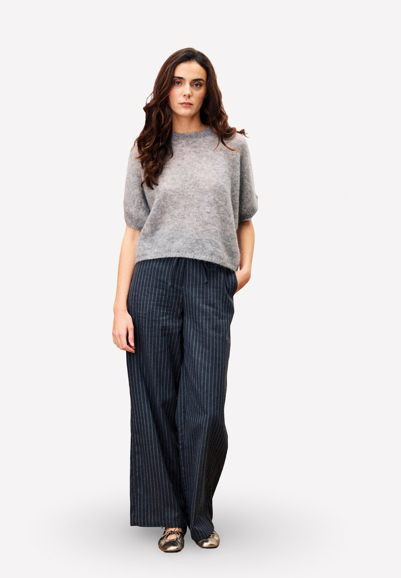 Grijze, fuzzy gebreide trui met korte mouwen gecombineerd met donkerblauwe, wijde gestreepte broek en metalen platte schoenen. Eenvoudig, ontspannen fit ontwerp.