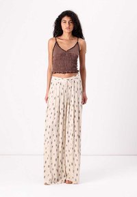 Top court smocké marron associé à un pantalon large crème avec un motif à losanges noirs, en tissu doux et avec une taille à cordon.