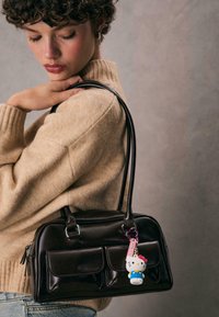 Czarna skórzana torebka z srebrnymi detalami, z dwiema przednimi kieszeniami i różowym breloczkiem z figurką Hello Kitty przymocowanym do uchwytu.