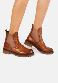 Botas de piel marrón hasta el tobillo con paneles elásticos laterales, puntera redondeada y suela de goma texturizada. Presentan un diseño holgado y altura hasta el tobillo.