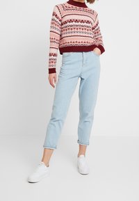 Maglione a maglia in bordeaux e rosa con motivi geometrici, abbinato a jeans azzurri con risvolto e sneakers bianche.