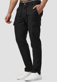 Black cargo pants with side pockets, drawstring waistband, and a slim fit, paired with white sneakers on a neutral background.