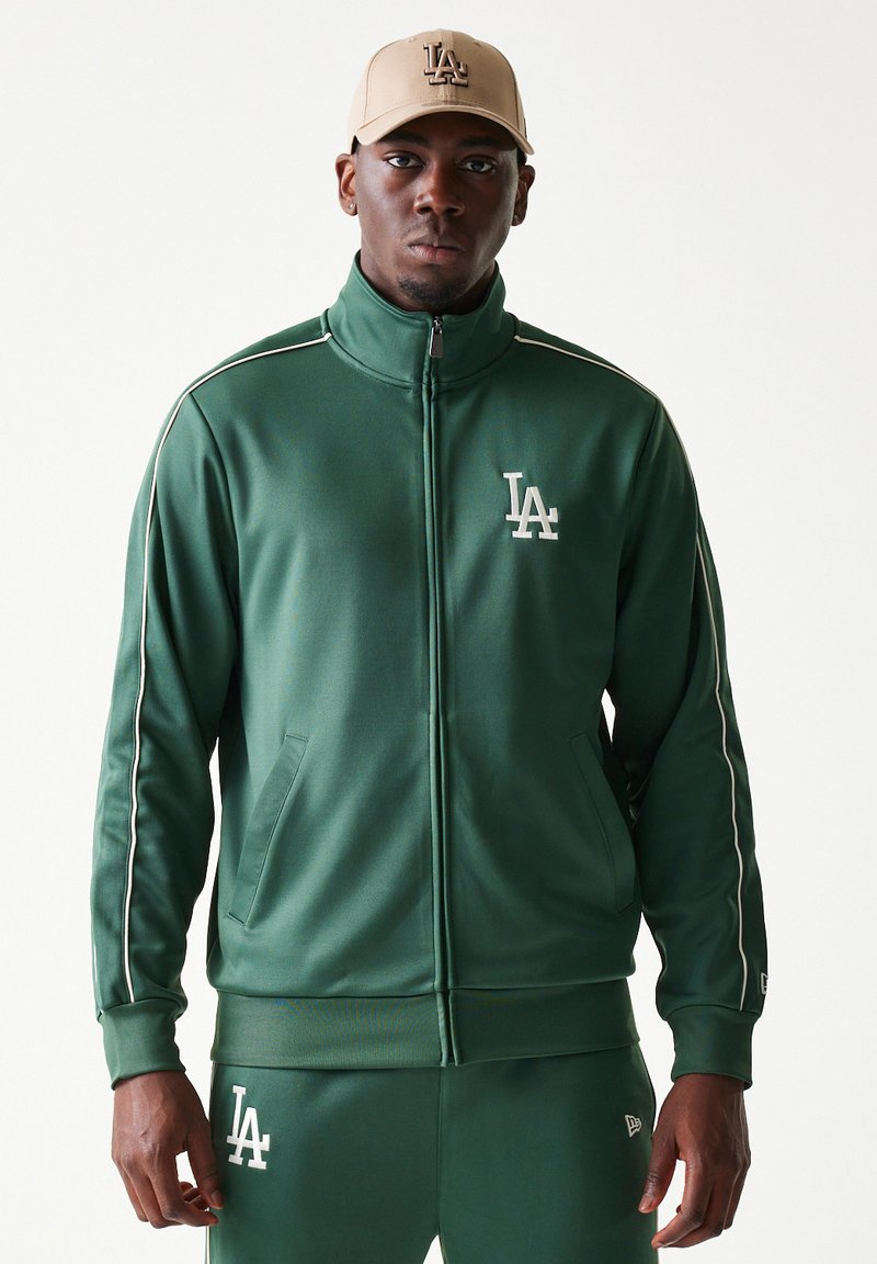 Πράσινο μπουφάν φόρμας με λευκές λεπτομέρειες και λογότυπο LA. Κατασκευασμένο από λείο, ελαστικό υλικό. Με φερμουάρ μπροστά και πλαϊνές τσέπες.