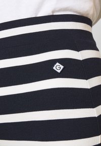 Närbild av en marinblå och vit randig trikåkjol i midjan med en liten broderad diamantsymbollogotyp.