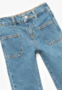 Jeans de denim azul claro con cintura alta, costuras naranjas, bolsillos delanteros y traseros, y un cierre de botón metálico único en la cintura.