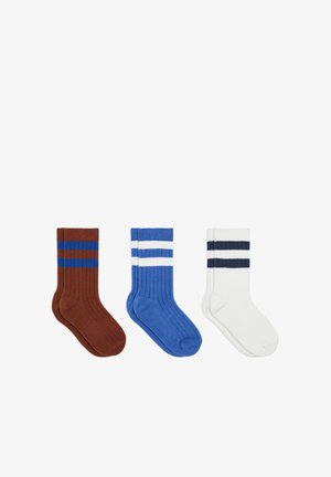 Trois paires de chaussettes à côtes montantes en marron avec des rayures bleues, bleu avec des rayures blanches, et blanc avec des rayures noires, posées à plat côte à côte.