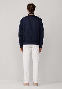 Chaqueta bomber de color navy con un cuello en contraste color beige, que cuenta con un tejido texturizado, puños elásticos y pantalones blancos a juego.