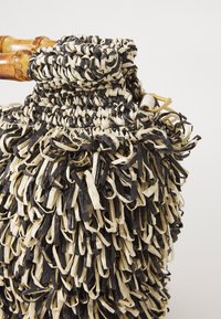 Borsa a tracolla intrecciata nera e crema con superficie testurizzata e manico in bambù, caratterizzata da una parte superiore arricciata e dettagli in metallo dorato.