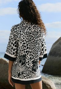 Kimonový plážový přehoz s leopardím potiskem v černobílé barvě, s krátkými rukávy, výstřihem do V a výraznými detaily leopardí grafiky.