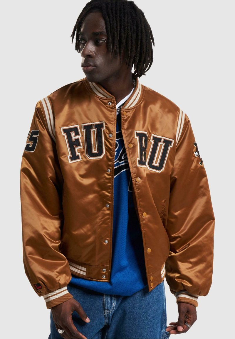 Brun satin bomberjakke med "FURRU" bogstaver, trykknapper, stribede ribkantmanchetter og en afslappet pasform, båret over en blå skjorte.