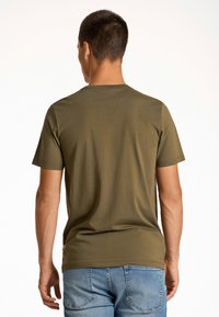 Camiseta de algodón verde oliva con cuello redondo y mangas cortas. Textura suave y corte relajado, combinada con pantalones cortos de mezclilla azul claro.