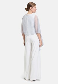 Haut léger bleu clair en tulle avec des manches texturées et superposées, associé à un pantalon large blanc, créant une silhouette fluide.