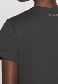 Charcoal šedé tričko s krátkými rukávy, které má jemnou texturu a nenápadné logo "PINKO" na zadní straně poblíž výstřihu.
