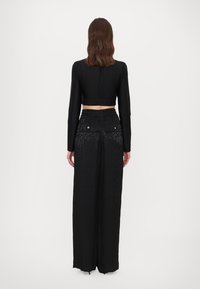 Zwarte cropped top met lange mouwen, gecombineerd met hoge taille, wijde zwarte broek met een subtiele luipaardprint en een elastische tailleband.