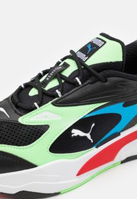 Chaussure de sport noire, verte, bleue et rouge en matériaux en mesh et synthétiques ; présente des surfaces texturées et le logo Puma reconnaissable.