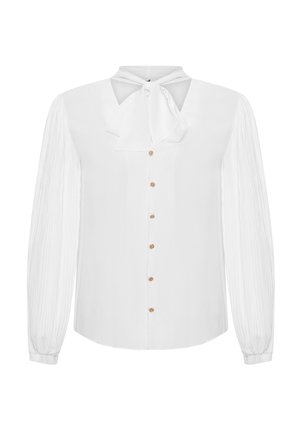 Blusa blanca de manga larga con cuello de lazo, cierre frontal de botones y mangas texturizadas. Presenta detalles de botones dorados a lo largo de la tapeta.