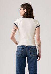 Cremefarvet top med raglanærmer og marineblå kant, tætsiddende design; bæres med medium-høj blå denim jeans med to baglommer og syninger.