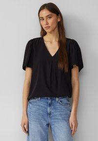 Blouse noire à col en V avec de courtes manches bouffantes, en tissu lisse. Assortie avec un jean en denim bleu clair pour créer un contraste.