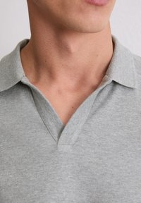 Grau Polohemd mit V-Ausschnitt, aus feinem strukturiertem Stoff gefertigt. Verfügt über einen klassischen Schnitt und dezente Nähte am Kragen.