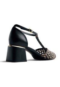 Sandalia de tacón de cuero negro con un tacón grueso acentuado en dorado, que cuenta con una parte superior de tejido trenzado y una correa ajustable en el tobillo para un ajuste seguro.