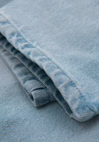 Tela de mezclilla azul claro, doblada con una textura en relieve visible y costuras prominentes, mostrando un acabado suave y liso.