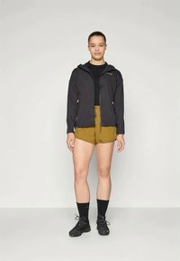 Čierna ľahká bunda s kapucňou, spárovaná s olivovo-zelenými šortkami. Model má na sebe čierne tričko, čierne ponožky a tmavé topánky.