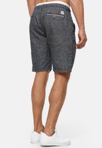 Shorts gris en tissu texturé, dotés d'une poche arrière avec un bouton et d'un accent rayé contrastant. Portés avec des baskets blanches.