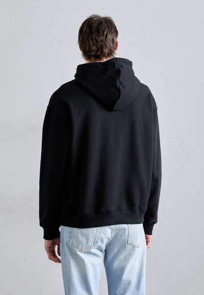 Black hooded sweatshirt made of soft fabric, featuring a relaxed fit and ribbed cuffs and hem. Worn with light blue jeans.