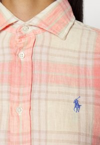 Camisa de botones en tejido ligero con un patrón de cuadros en rosa y beige. Pequeño logo de polo azul en el lado izquierdo del pecho. Detalle de cuello clásico.