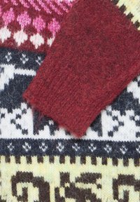 Gros plan de pulls en laine avec des motifs géométriques multicolores et une manche tricotée rouge texturée chevauchant une section blanche et noire à motifs.