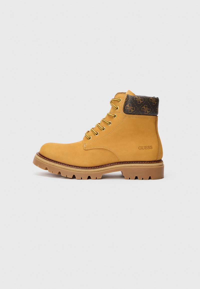 Botte en cuir tan à lacets avec semelle robuste, col rembourré brun foncé imprimé de logos, et "GUESS" embossé sur le côté.