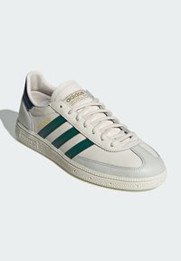 Białe skórzane sneakersy z zielonymi paskami, szarymi akcentami i teksturowaną podeszwą. Posiadają wyściełany kołnierz oraz branding na języku.