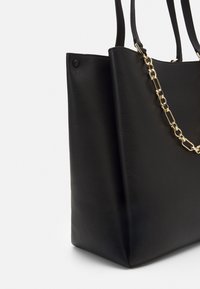 Czarna skórzana torba na ramię o teksturowanym wykończeniu, z dwiema rączkami oraz złotym łańcuszkiem po jednej stronie.