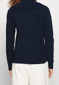 Pullover blu navy a maniche lunghe con un design aderente. Texture morbida e cuciture senza soluzione di continuità sulla schiena. Stile minimalista senza loghi visibili.