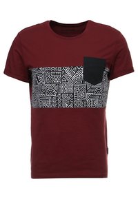 Camiseta roja de manga corta con un panel de patrón geométrico negro en el pecho y un bolsillo negro en el lado izquierdo. Tela de algodón.