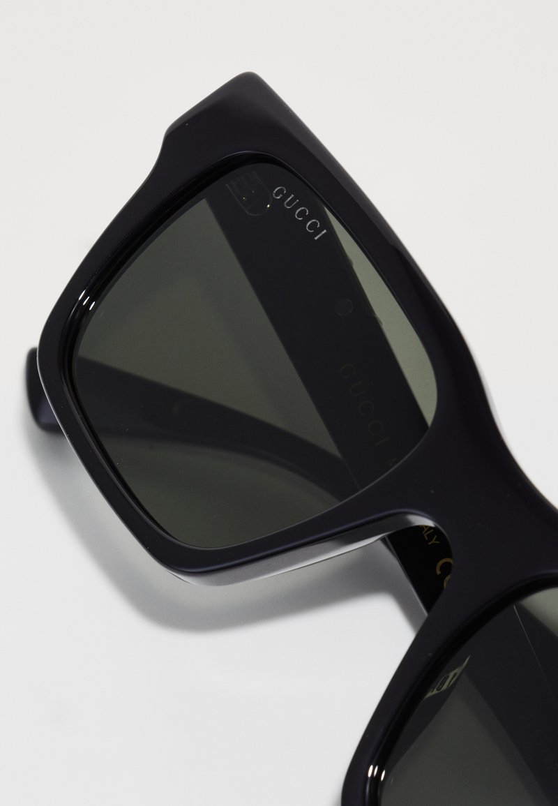 Black square sunglasses with dark lenses, featuring embossed logo on the frame. Smooth texture with simple, bold design.
