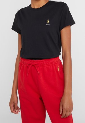 Zwart katoenen T-shirt met korte mouwen, voorzien van een klein goudkleurig geborduurd logo. Gecombineerd met rode joggingbroek met elastische tailleband en logo.