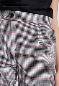 Kalhoty s černo-bílým vzorem houndstooth, s červenými a hnědými mřížkami. Obsahují sklady a jeden černý knoflík v pase.