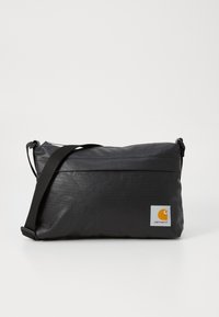 Borsa messenger in tessuto nero con chiusura lampo, tracolla regolabile e logo Carhartt arancione su sfondo bianco. Texture liscia, forma rettangolare.