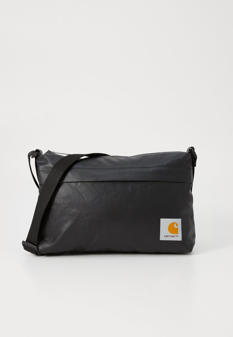 Sac messager en tissu noir avec fermeture éclair, bandoulière réglable et logo Carhartt orange sur fond blanc. Texture lisse, forme rectangulaire.